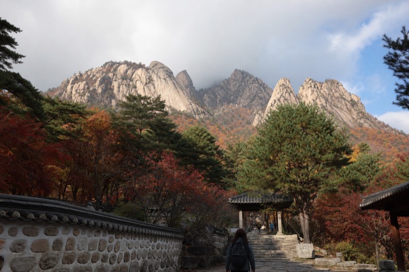 Steep granite peaks above a valley in a Korean national park, autumn colour on the lower slopes and a temple roof below