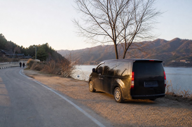 A plain dark people carrier waiting on a quiet country road beside a river, ready for a private day trip